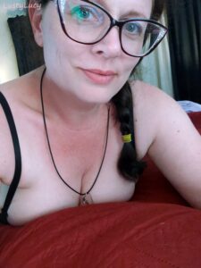 LustyLucy is a cam model smiling at the camera wearing glasses and a smile and showing off her cleavage with side braided hair.