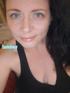 Cam model and content creator LustyLucy smiling slightly with her lips and green eyes. She has pretty green eyeliner on and her shirt is lopsided.